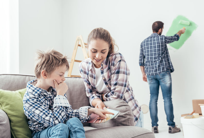 family, mother, father, husband, wife, couple, man, woman, son, child, boy, brunette, plaid, flannel, jeans, distressed jeans, paint, green, green paint, painting, wall, ladder, wood, wooden ladder, couch, gray, green, pillow